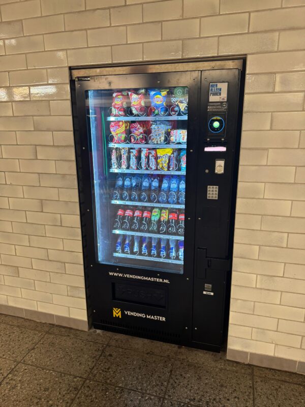 Ingebouwde vendingmachine op Amsterdam Centraal NS Station, strak geïntegreerd in de muur voor een nette afwerking en een toegankelijke 24/7 vendingoplossing voor reizigers