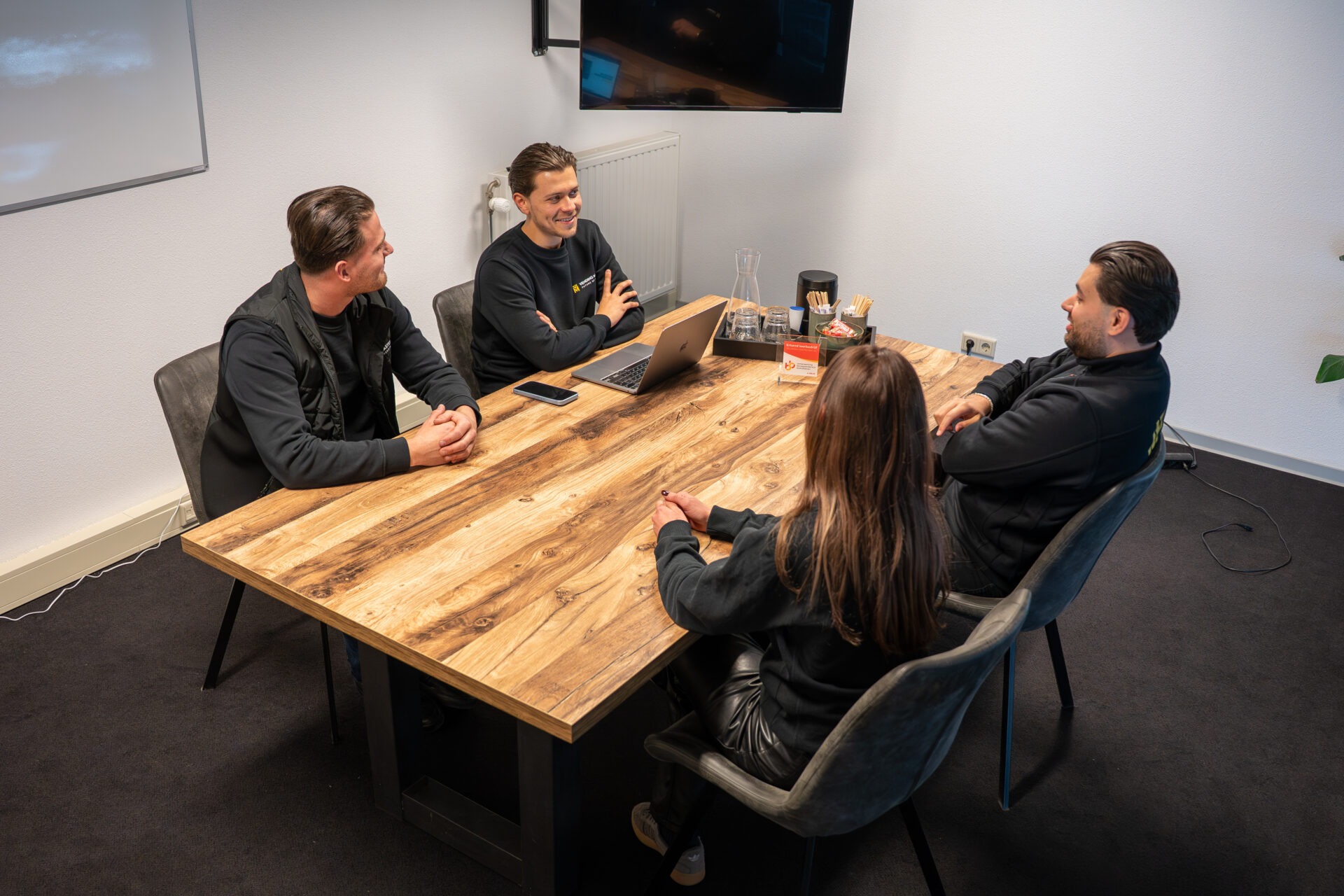Vier medewerkers in kantoor die tijdens een marketingoverleg aan tafel nieuwe marketing en communicatie ideeën bespreken
