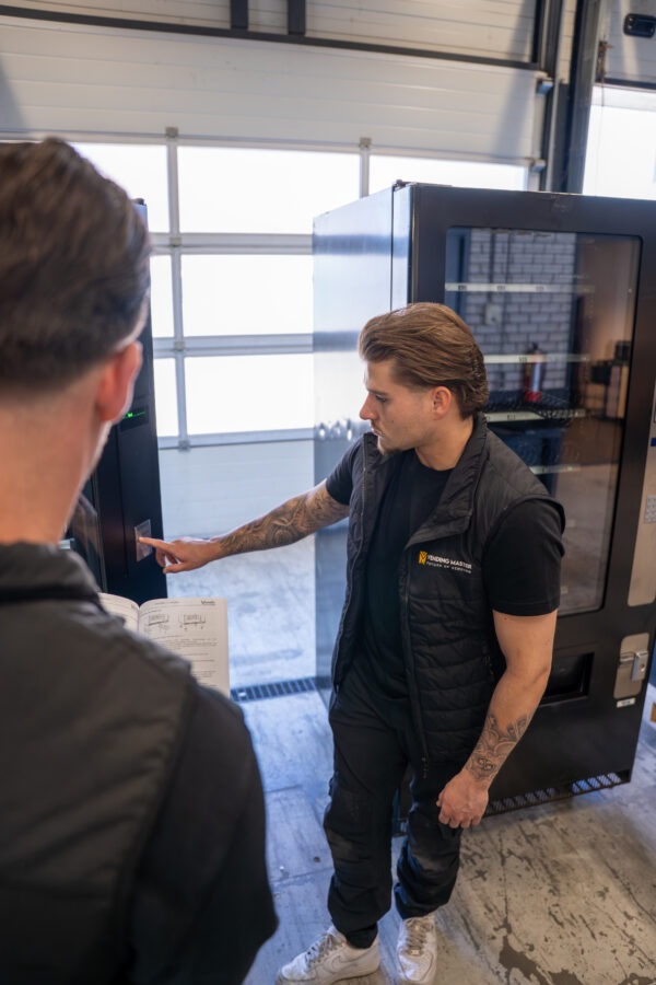 Monteur van Vending Master geeft op locatie professionele uitleg over de installatie en werking van een vendingautomaat aan klant, inclusief duidelijke instructies en advies voor optimaal gebruik